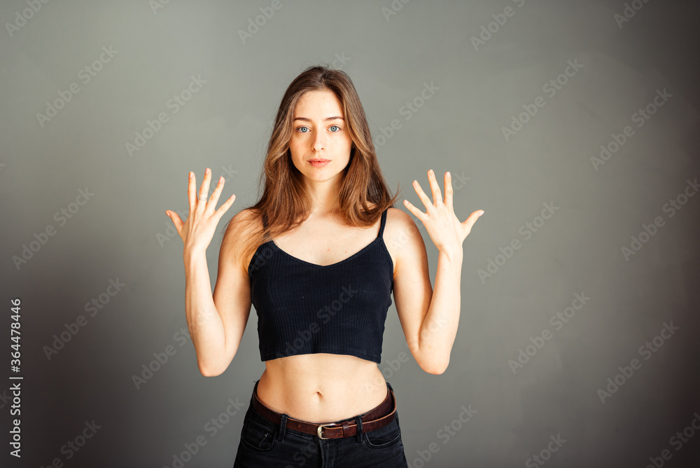 A girl in a black top with her hair with both hands shows the boats. Show clean hands insulator on a gray background. Without makeup, without retouching. A girl in a black top with her hair with both hands shows the boats. Show clean hands insulator on a gray background. Without makeup, without retouching.