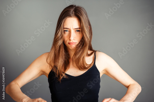 The girl with her hair in a black top looks thoughtfully to the side. To be upset, thoughtful, serious. On a gray background. Without makeup, without retouching.