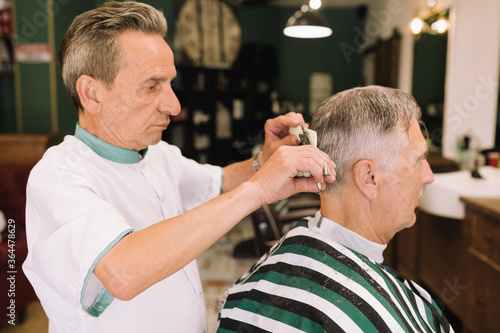 elderly barber cutting the hair of a gentleman in a stylish barber shop