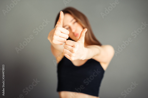 Girl in a black top with her hair shows thumb up. On a gray background. Without makeup, without retouching.