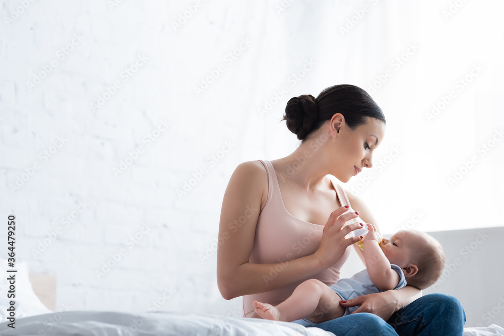 beautiful woman feeding cute infant son while holding baby bottle beautiful woman feeding cute infant son while holding baby bottle