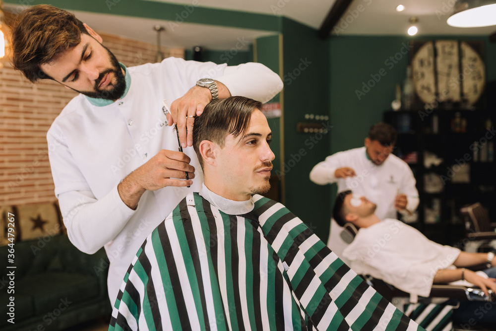 handsome barber cutting the hair of a young brunette in the barber shop handsome barber cutting the hair of a young brunette in the barber shop