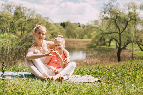 A young mother and daughter in sportswear do yoga together in a Park. The concept of a family holiday. Sports, fitness, meditation