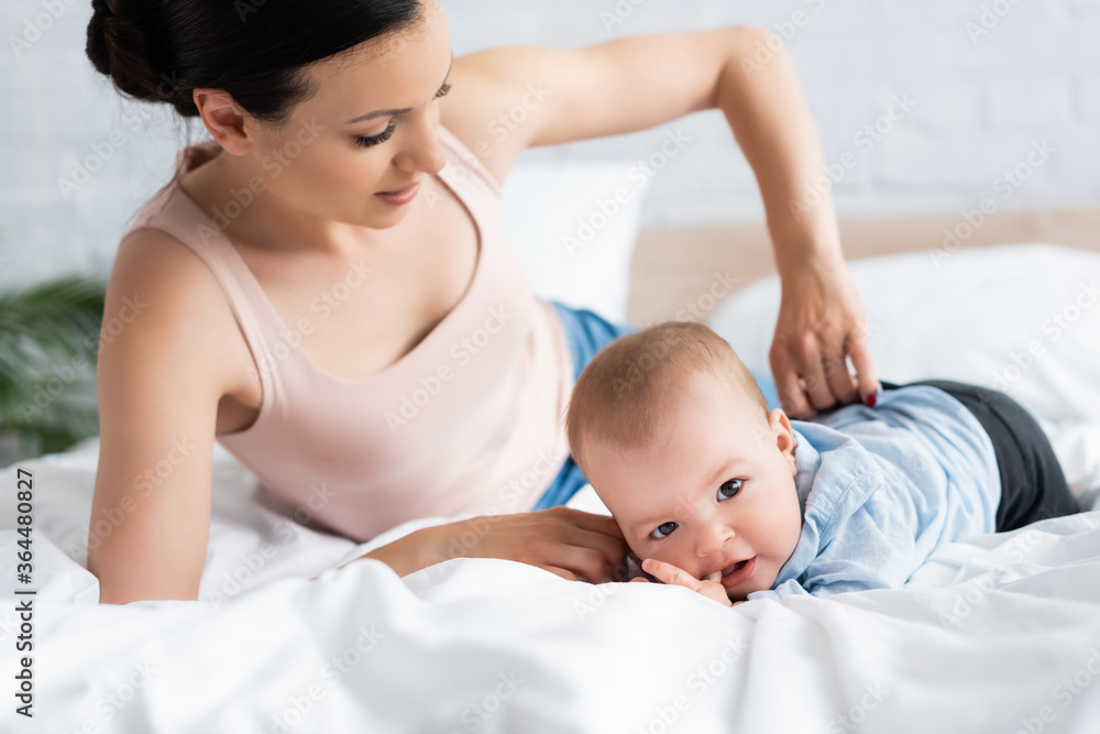 selective focus of mother touching baby clothing on infant son lying on bed selective focus of mother touching baby clothing on infant son lying on bed
