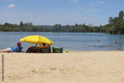 personnes sous un parasol jaune eu bord d'un lac 