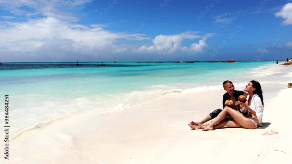 Unforgettable honeymoon of young couple in love, pretty wife in white bikini sitting on white sand and tasting exotic beverage. Summer relax at the maldives resort, couple enjoying summer vacations Unforgettable honeymoon of young couple in love, pretty wife in white bikini sitting on white sand and tasting exotic beverage. Summer relax at the maldives resort, couple enjoying summer vacations