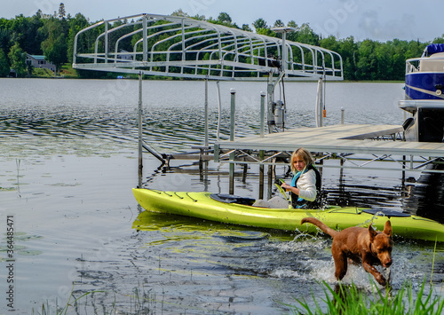 A young girl in a yellow kayak on a lake with her dog.