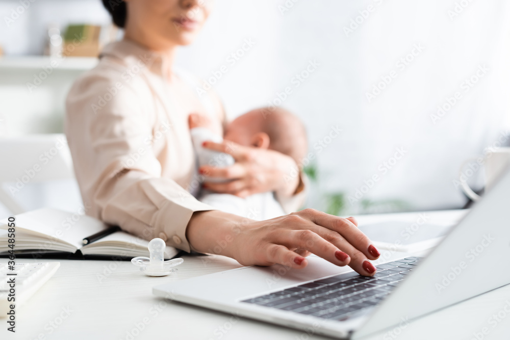Fototapeta premium selective focus of mother breastfeeding infant son while working from home with laptop