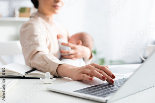 selective focus of mother breastfeeding infant son while working from home with laptop