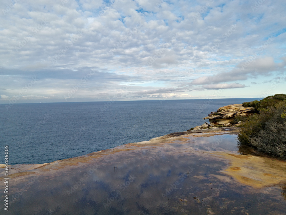 Beautiful coastal trail with colorful rock formations and reflections of blue sky on water puddles near Wattamolla Beach, Royal National Park, New South Wales, Australia