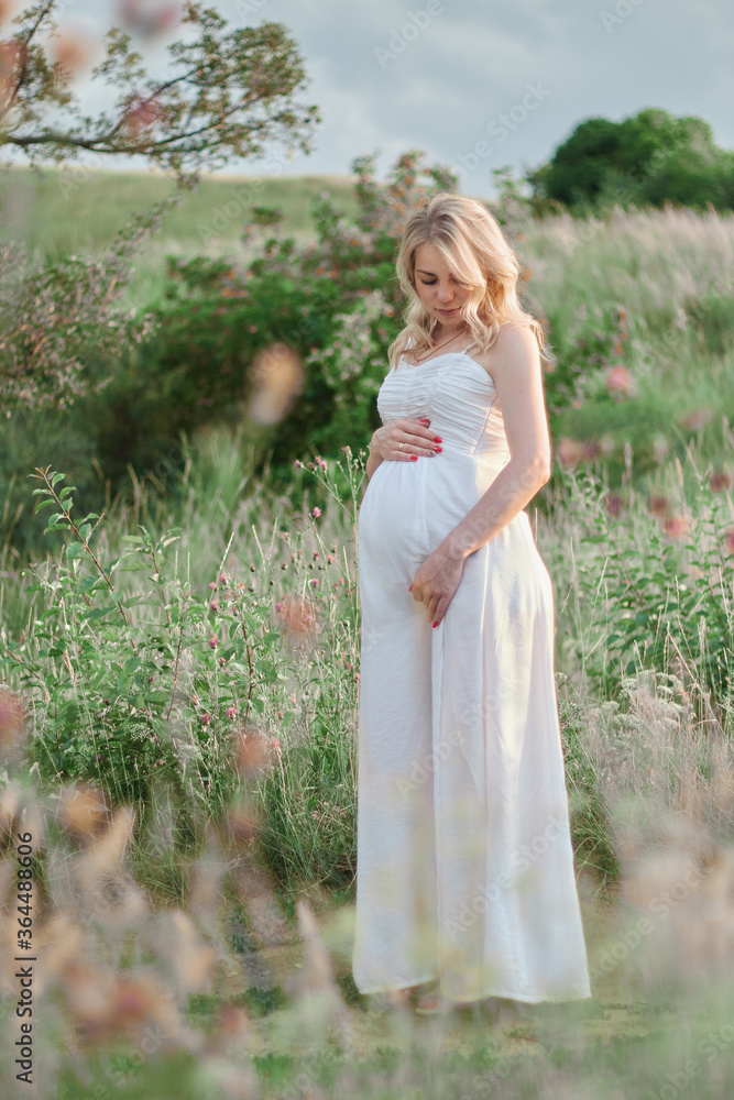 Young blonde Russian pregnant girl in a white dress on a background of nature Young blonde Russian pregnant girl in a white dress on a background of nature