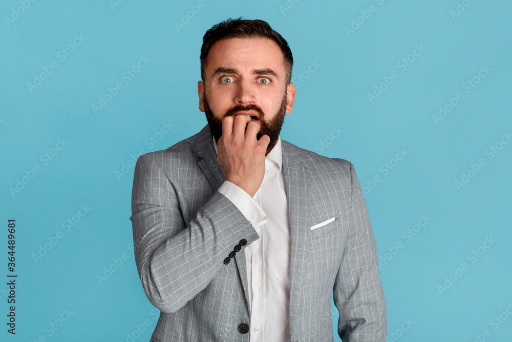 Stress management. Scared businessman biting fingernails in panic on blue background Stress management. Scared businessman biting fingernails in panic on blue background