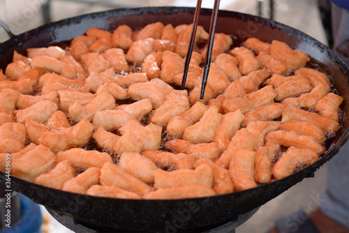 Many deep-fried doughstick are in a large iron pan, With boiling oil. photo