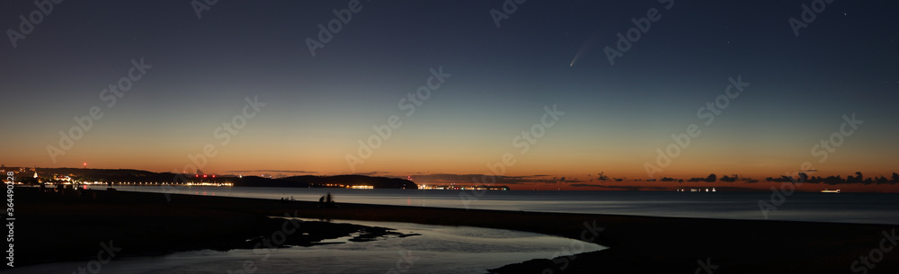 Gdansk, Poland - July 11 2020 : comet C/2020 F3 NEOWISE in the summer sky as seen from Gdansk. Panorama of coastline of Gulf if Gdansk with city lights of  Sopot and Gdynia on the horizon.
