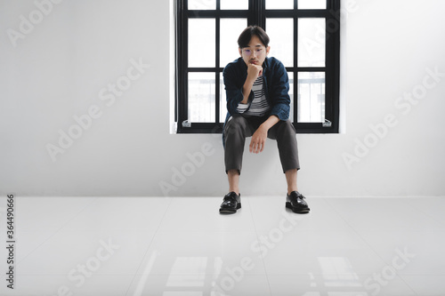 Young hipster asian man thinkong and sitting side window in white room