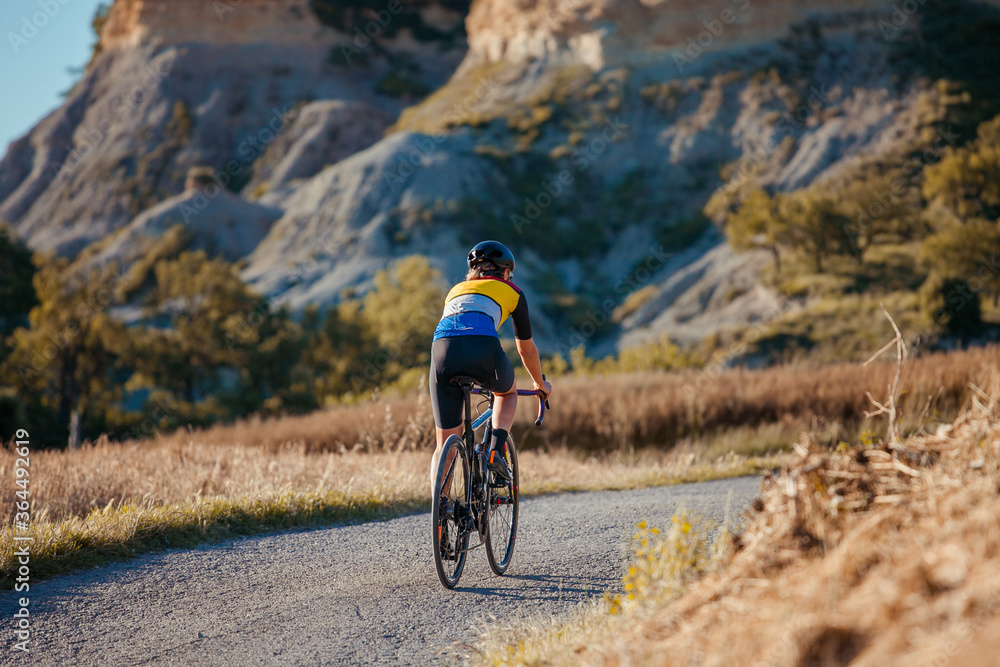 Fototapeta premium Back view of a cyclist girl pedaling on her bicycle in a beautiful countryside setting.