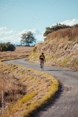 Fototapeta Naklejka Na Ścianę i Meble -  Female professional cyclist quickly descends the slope of a beautiful countryside road.