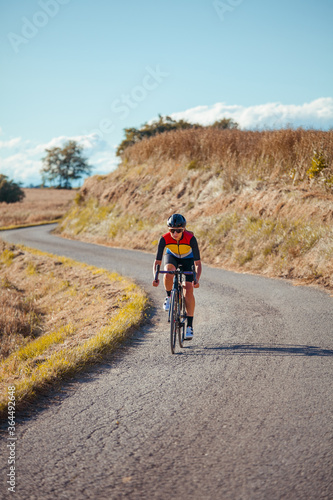 Female professional cyclist descends fast the slope of a beautiful countryside road.