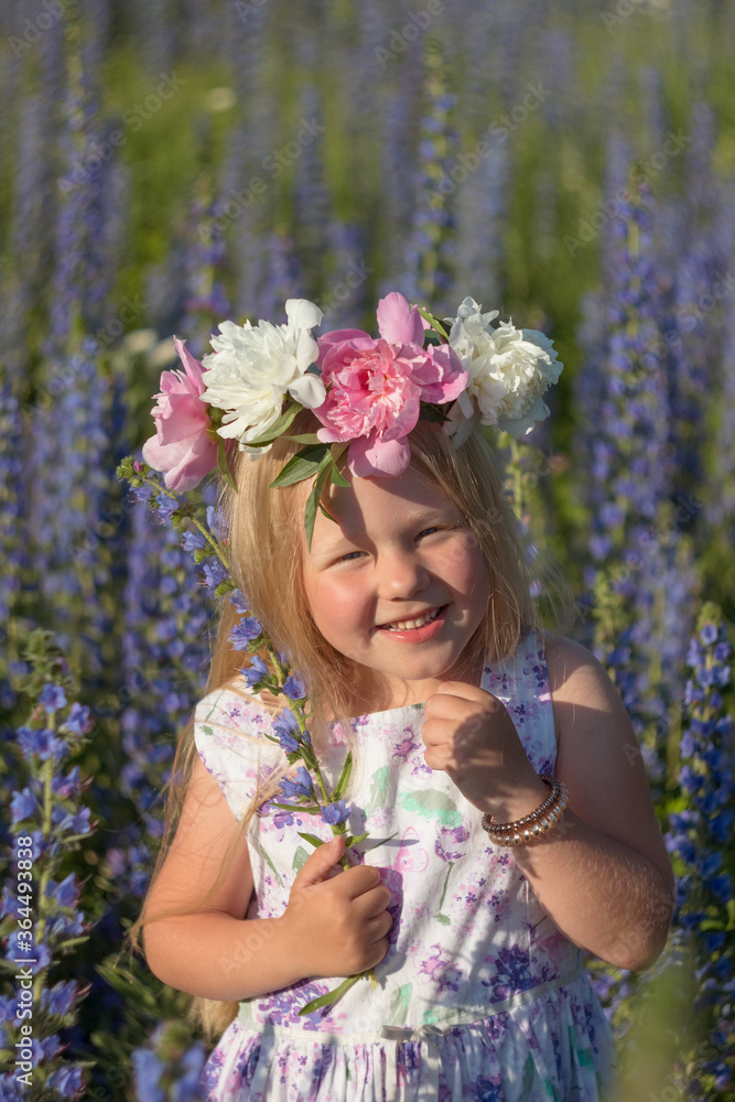 Obraz premium Little beautiful girl in a flower field on a sunny summer day during summer vacation. A girl with long hair smiles and laughs. Girl with a wreath on her head. Selective focus image.