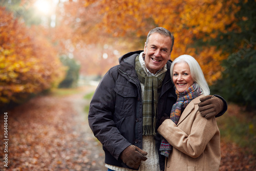 Portrait Of Loving Senior Couple Hugging As They Walk Along Autumn Woodland Path Through Trees