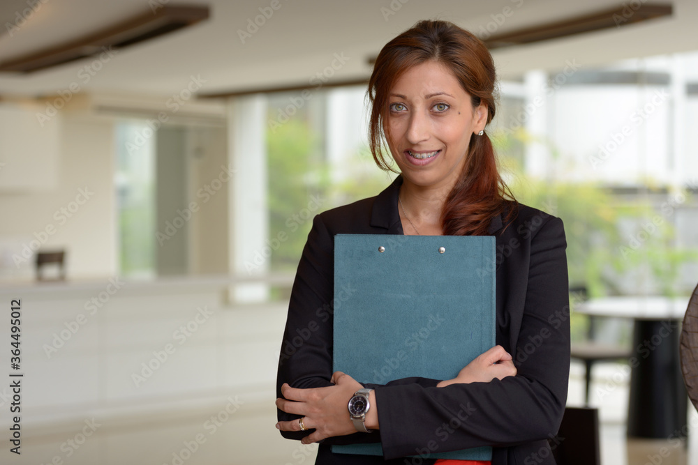 Happy Hispanic businesswoman holding clipboard inside the office building Happy Hispanic businesswoman holding clipboard inside the office building