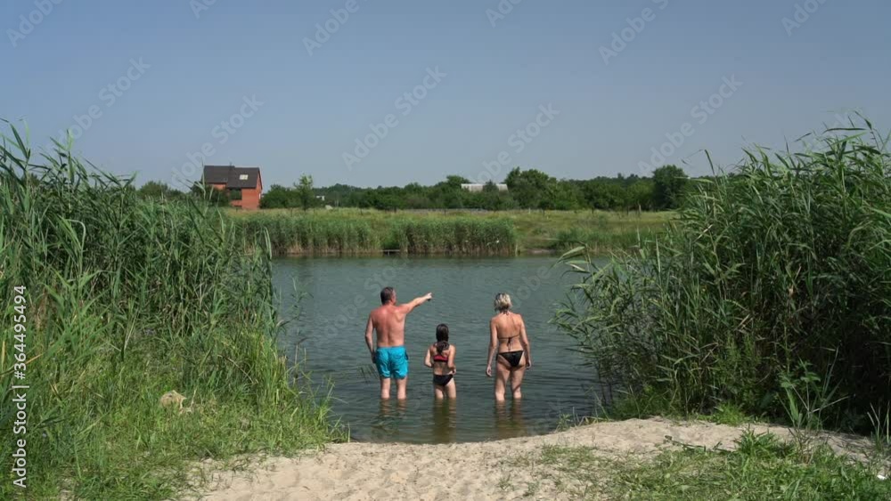 Family with daughter wearing swimsuits standing in river shallow water and talking Family with daughter wearing swimsuits standing in river shallow water and talking