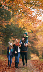 Family Walking Along Autumn Woodland Path With Father Carrying Son On Shoulders