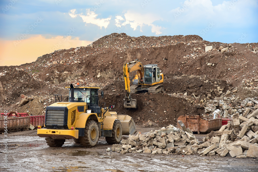 Obraz premium Front end loader and excavator at landfill for disposal of construction waste. Gravel and concrete crushing. Recycling old concrete and asphalt from demolition. Salvaging, removal building materials