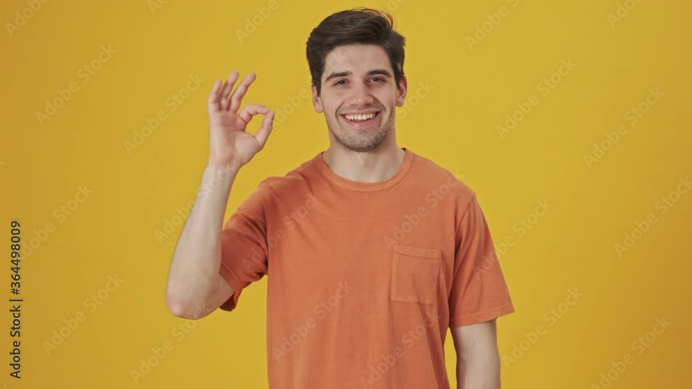 Smiling handsome man wearing in t-shirt showing ok sign gesture at the camera over yellow background Smiling handsome man wearing in t-shirt showing ok sign gesture at the camera over yellow background