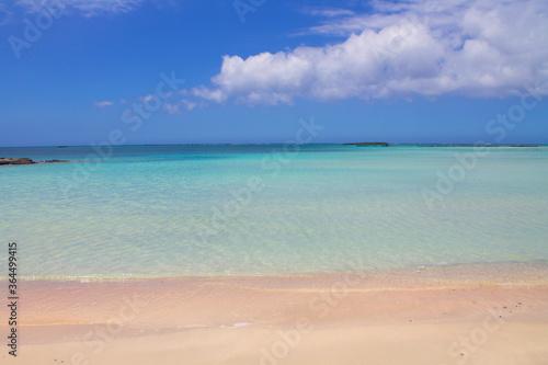 Beach with pink sand and turquoise water and clouds in blue sky. © Alena