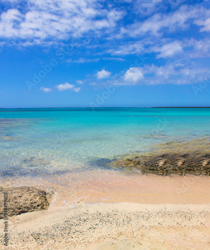 Beach with pink sand, stones and turquoise water and clouds in blue sky. © Alena