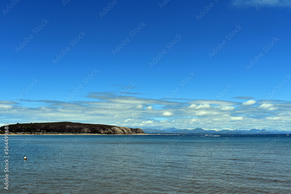 The waterfront at the beautiful Welsh seaside resort of Abersoch.  View over the Irish sea to the horizon and the cliffs of the bay.  Blue skies, copy space.