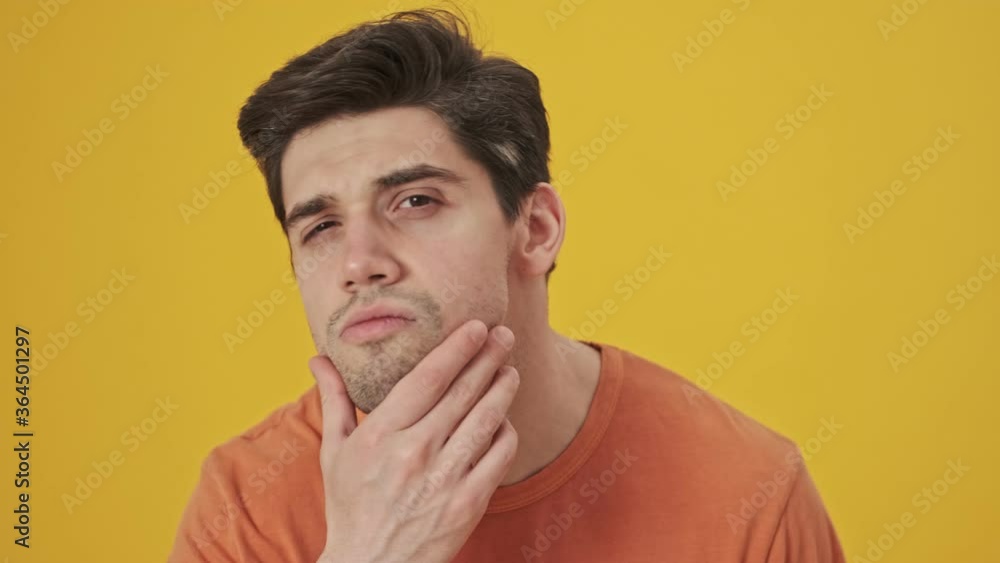 Close up view of Smiling handsome man wearing in t-shirt touching his face and hair while looking at the mirror over yellow background Close up view of Smiling handsome man wearing in t-shirt touching his face and hair while looking at the mirror over yellow background