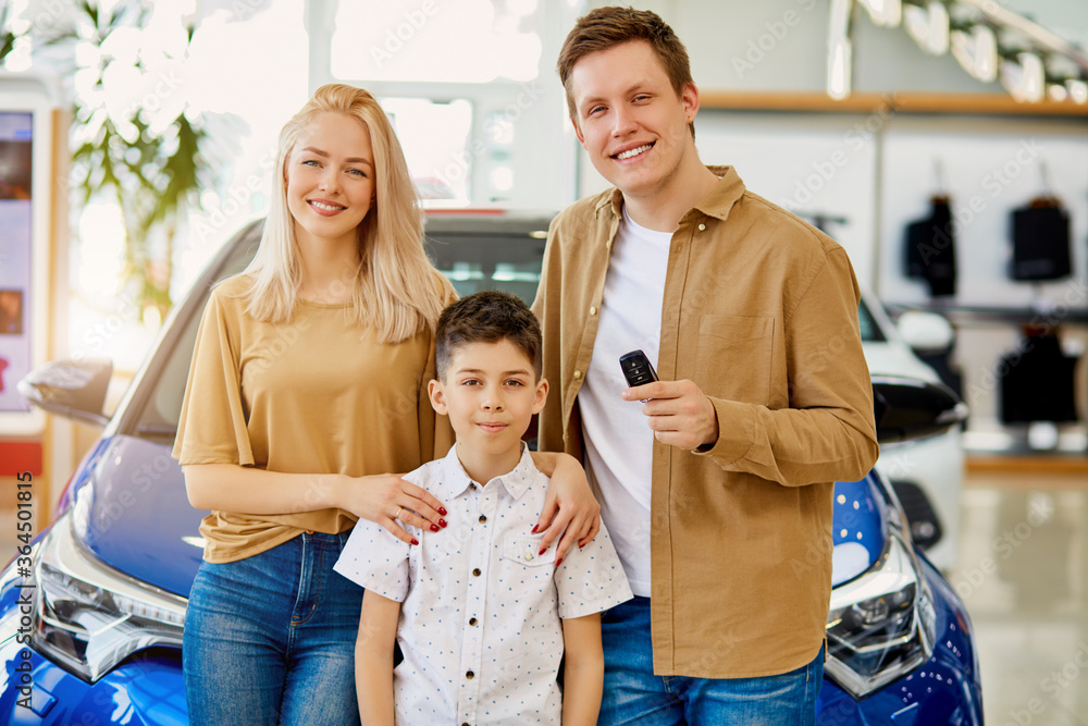 portrait of happy smiling family holding car keys in dealership, man woman and child boy look at camera and smile. beautiful car in the background portrait of happy smiling family holding car keys in dealership, man woman and child boy look at camera and smile. beautiful car in the background