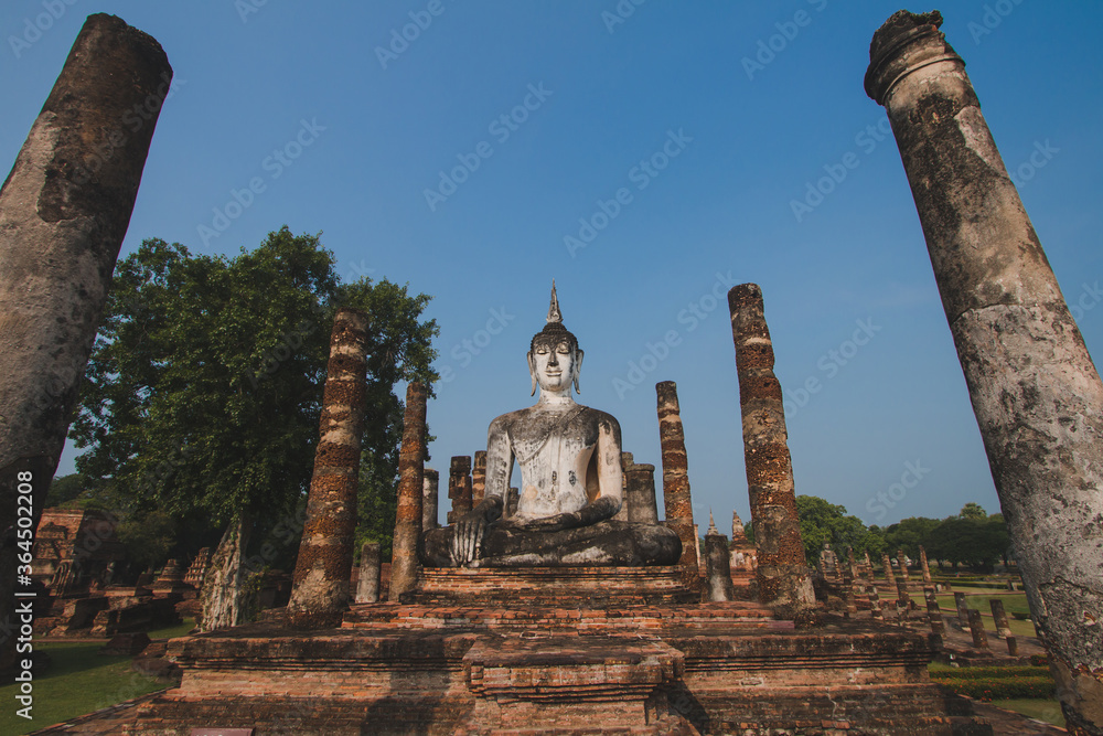 The large old Buddha statue Enshrined stands majestically in the Sukhothai Historical Park. Amid the orange-coloured sky during the evening, Sukhothai Province, Thailand