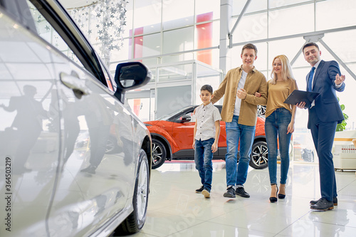 young confident salesman represent new auto for clients, caucasian family came to get new car, they get consultation and help by responsive salesman