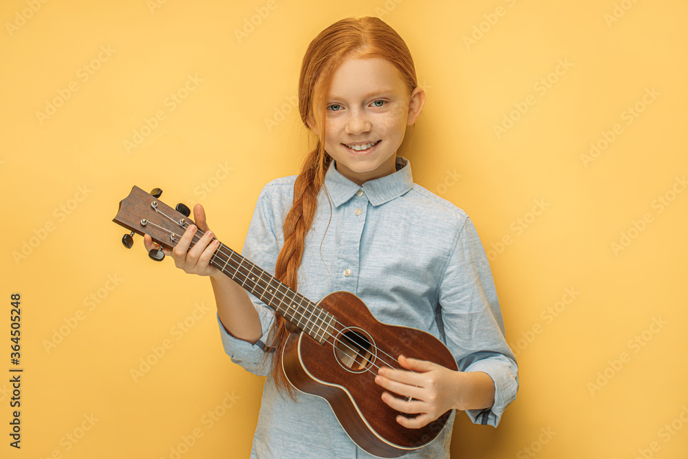 adorable caucasian teen girl with natural red hair holding ukulele in hands, she enjoy playing in such unusual type of instruments ukulele, small guitar. music, people, children concept adorable caucasian teen girl with natural red hair holding ukulele in hands, she enjoy playing in such unusual type of instruments ukulele, small guitar. music, people, children concept