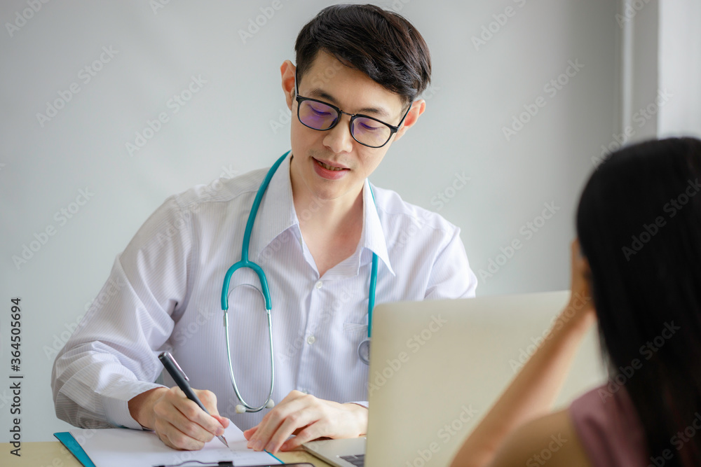 Young Asian male doctor is recording a medical history on the clipboard and explaining something to the female patient. Medical and health care concepts Young Asian male doctor is recording a medical history on the clipboard and explaining something to the female patient. Medical and health care concepts