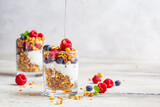 Yogurt parfait with granola, raspberries, honey and blueberries in glasses, light gray background, copy space. Healthy breakfast concept.