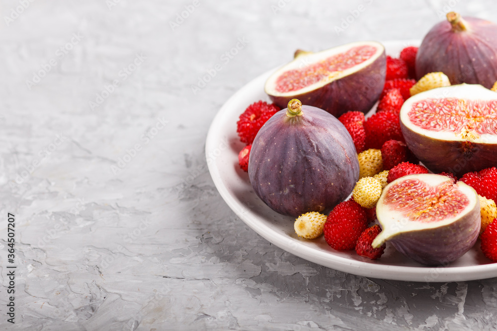 Fresh figs, strawberries and raspberries on white plate on gray concrete background. side view, copy space.