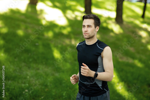 Summer sport. Guy in sportswear with fitness tracker runs in park