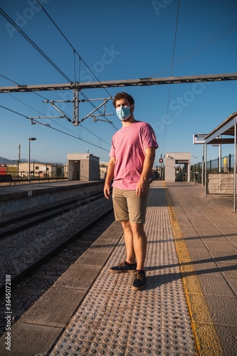 Vertical photo of a young man with a mask waiting on a station platform © Daniel