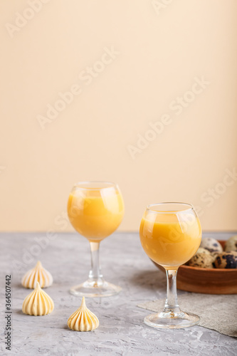 Sweet egg liqueur in glass with quail eggs and meringues on a gray and orange background. Side view