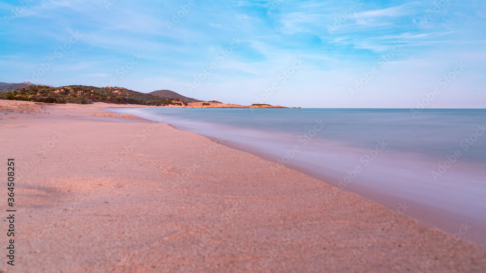 Panoramic view of a long exposure sunset shot of Su Giudeu beach, in Chia, Cagliari, Italy, with seashore view, mountains and soft waves