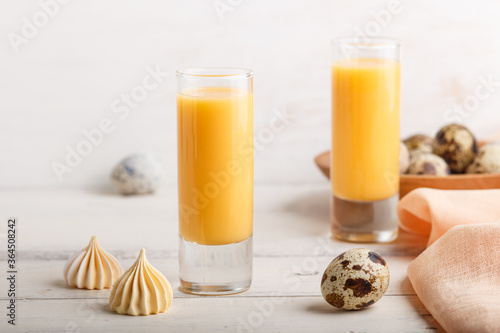 Sweet egg liqueur in glass with quail eggs and meringues on white wooden background. Side view, close up. photo