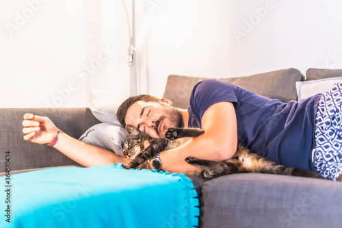 A young Caucasian man sleeping embraced on the sofa with his best friend the cat, housemate the precious animal.