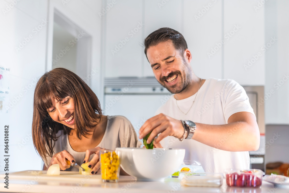 A Caucasian couple cooking together at home, cooking in confinement, cooking with the family. Coronavirus, covid-19. Preparing a salad, bride cutting onion and putting spinach