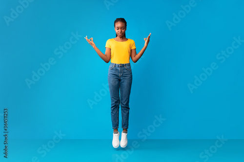 African American Millennial Girl Meditating In Mid-Air Over Blue Background
