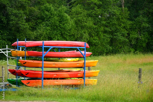 Close up on a set of colorful kayaks secured with a metal frame and ready for rental seen on a Polish countryside next to a dense forest or moor on a grass covered meadow or lawn in summer