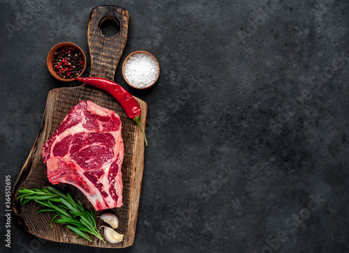 Raw cowboy steak. Marbled beef meat with spices on a stone background